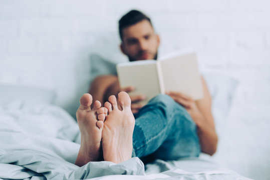 Selective Focus Of Man Reading Book In Bedroom At Home