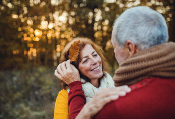 A senior couple standing in an autumn nature at sunset, looking at each other.