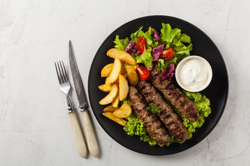 Traditional cevapcici served with baked potatoes. Flat lay. Stone background.