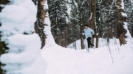 Young healthy man running in forest at winter