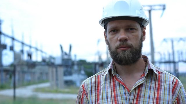 Station technical director with working drawings at nuclear power station. Worker in white helmet with engineering drawing near outdoor switchgear at nuclear power station