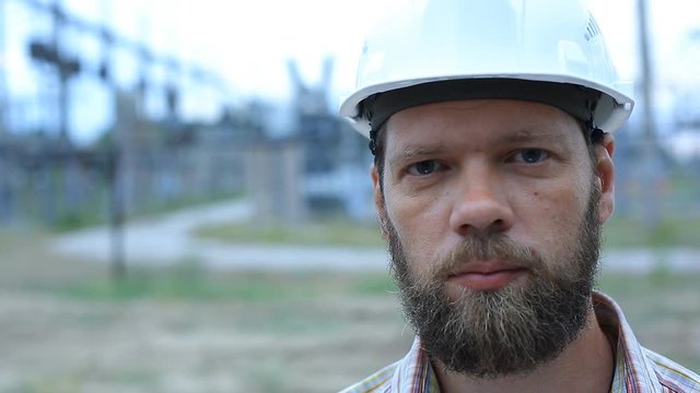 Station technical director with working drawings at nuclear power station. Worker in white helmet with engineering drawing near outdoor switchgear at nuclear power station