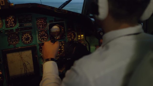 Over the shoulder shot of pilot in headset using yoke while flying airplane