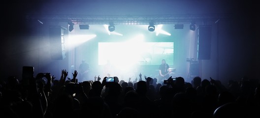 Crowd of fans with hands in the air watching a rock band concert.