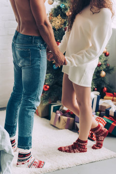 cropped image of couple holding hands of each other near christmas tree at home
