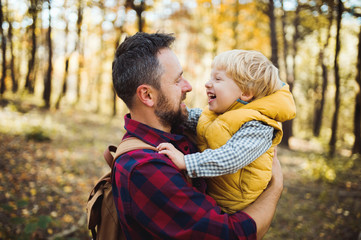 A mature father holding a toddler son in an autumn forest, talking.