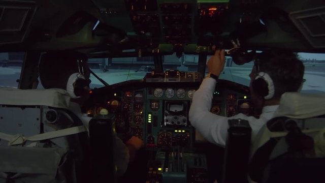 Medium shot from inside of cockpit: professional male pilots in headsets operating instrument panel and preparing for take-off as airplane moving along runway