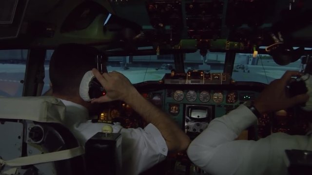 PAN shot of male pilots in headsets operating instrument panel in cockpit and preparing for flight