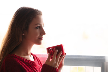 Girl holding cup in her hands in red knitted mittens