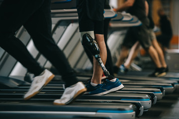 Fototapeta premium cropped shot of sportsman with artificial leg running on treadmill at gym with other people