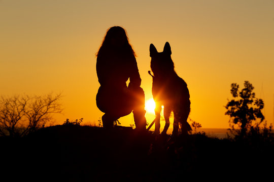 silhouette woman walking with a dog in the field at sunset, a girl in an autumn jacket on hill showing her pet target ahead on the nature