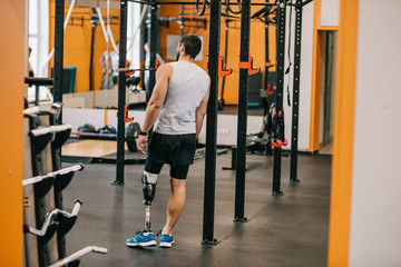 handsome young sportsman with artificial leg standing near gymnastics ladder at gym