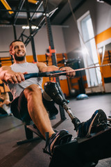 muscular young sportsman with artificial leg working out with rowing machine at gym