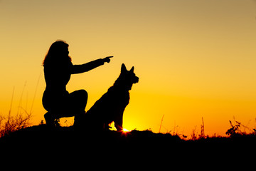 silhouette woman walking with a dog in the field at sunset, a girl showing her pet target ahead on the nature