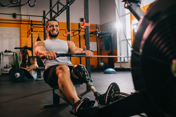 handsome young sportsman with artificial leg working out with rowing machine at gym