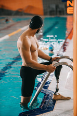 muscular young swimmer with artificial leg getting out of swimming pool - obrazy, fototapety, plakaty