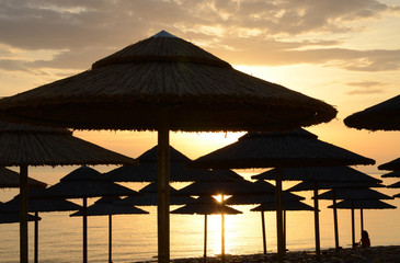 Beach straw umbrellas against the backdrop of a dawn sky on the shores of the Aegean Sea