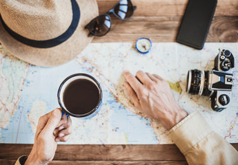 Fototapeta na wymiar Young traveller man discovering travel map and drinking coffee. Accessories and different objects on wooden background. Top view. Travel, tourism, vacations and active lifestyle concept. 