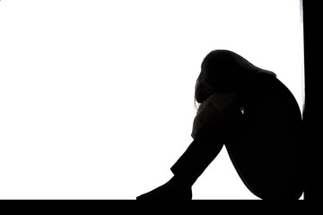 silhouette of a woman sitting on the floor in a corner on a white isolated background, a sad girl crying putting head on knees