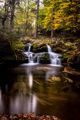 Fototapeta na wymiar cascadas de sedas en río en otoño con hojas y piedras