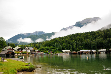 Fototapeta premium Houses and pier on the shore of Konigssee lake. Mountains with clouds in the background. Bavaria, Germany.