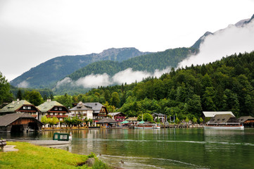 Obraz premium Houses and pier on the shore of Konigssee lake. Mountains with clouds in the background. Bavaria, Germany.