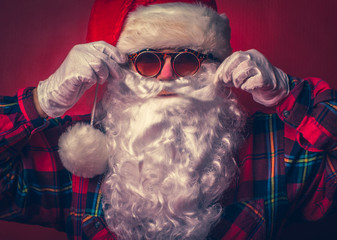 Close-up portrait of bearded Santa Claus in a hipster shirt and sunglasses.