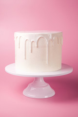 Simple white cake with white glaze on a pink background.