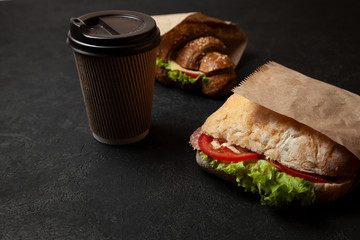 Sandwich and cup of coffee on black background. Morning breakfast or snack when hungry. Street food to go