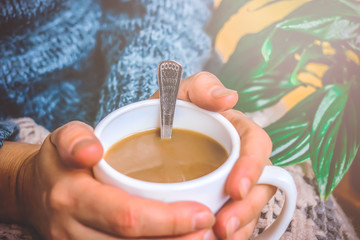 hands of a young woman holding a cup of coffee with milk. knitted clothes.