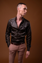 Young handsome androgynous businessman against brown background