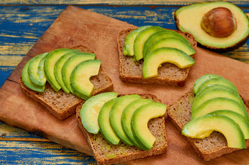 Healthy vegan breakfast - fresh sliced avocado on toast bread on the wooden board. Side view