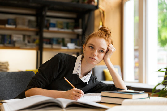 Image of beautiful student studying, while sitting at desk in college library with bookshelf background