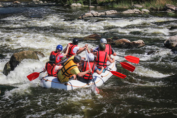 Group of men and women, enjoy water rafting activity at river. Extreme rafting.