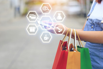 young woman hand holding smartphone with hologram and shopping bags with standing at the car parking lot, shopping concept