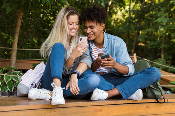 Happy young loving couple using mobile phone outdoors in park.