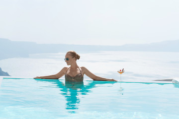 Young woman relaxing in the pool with a gorgeous view on Santorini.