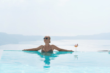 Young woman relaxing in the pool with a gorgeous view on Santorini.