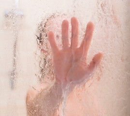 Fototapeta premium Female hand on the blurry glass of the shower door.