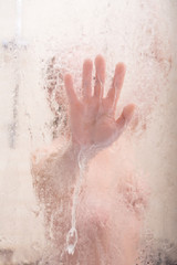 An unrecognizable woman touches the blurred glass while taking a shower.