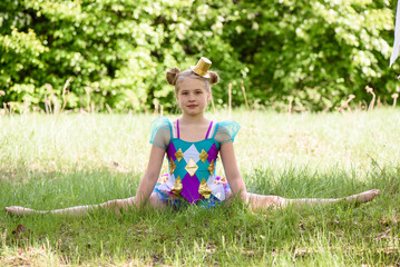 Young sporty blond girl sitting on grass in the park,gymnastic splits