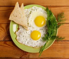 Fried eggs of 2 eggs with a piece of bread, dill on the table.