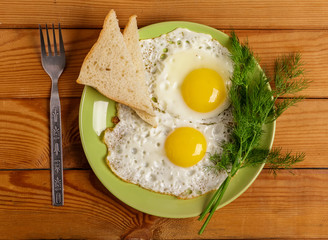 Fried eggs of 2 eggs with a piece of bread, dill on the table.