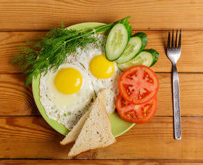 Fried eggs, pieces of vegetables, bread and fork on the table.