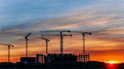 Construction cranes working at sunset, workers engaged in construction, time lapse