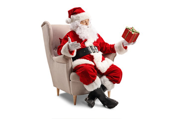 Santa Claus sitting in an armchair and holding a present