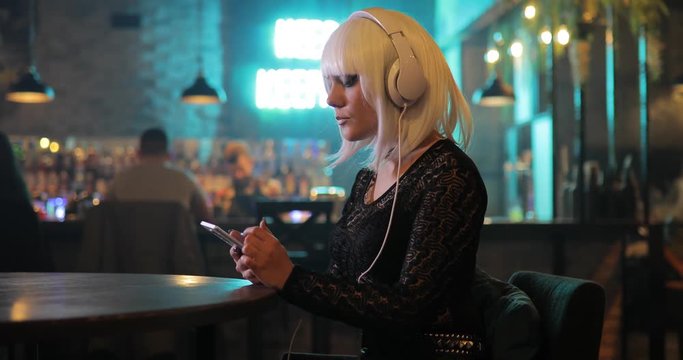 Sexy unusual girl in white wig listening to music with headphones in bar