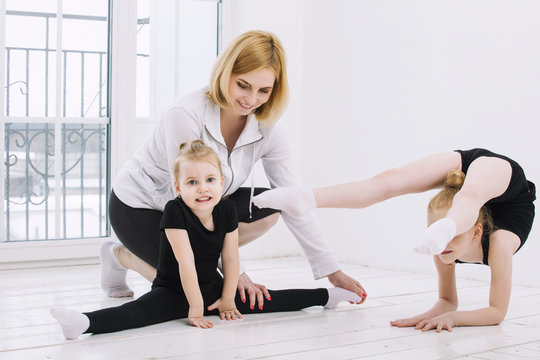 Little girl girls gymnasts and dancer doing stretching with a female coach in a bright room happy and cute