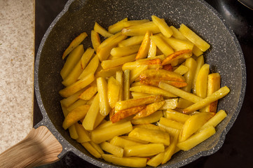 Close up, macro. Fried potatoes. Slices of shredded potatoes are fried in vegetable oil in a gray marble griddle.