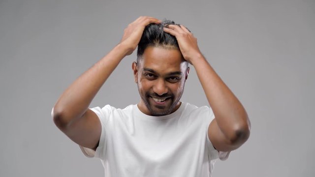 grooming, hairstyling and people concept - smiling young indian man applying hair wax or styling gel over gray background
